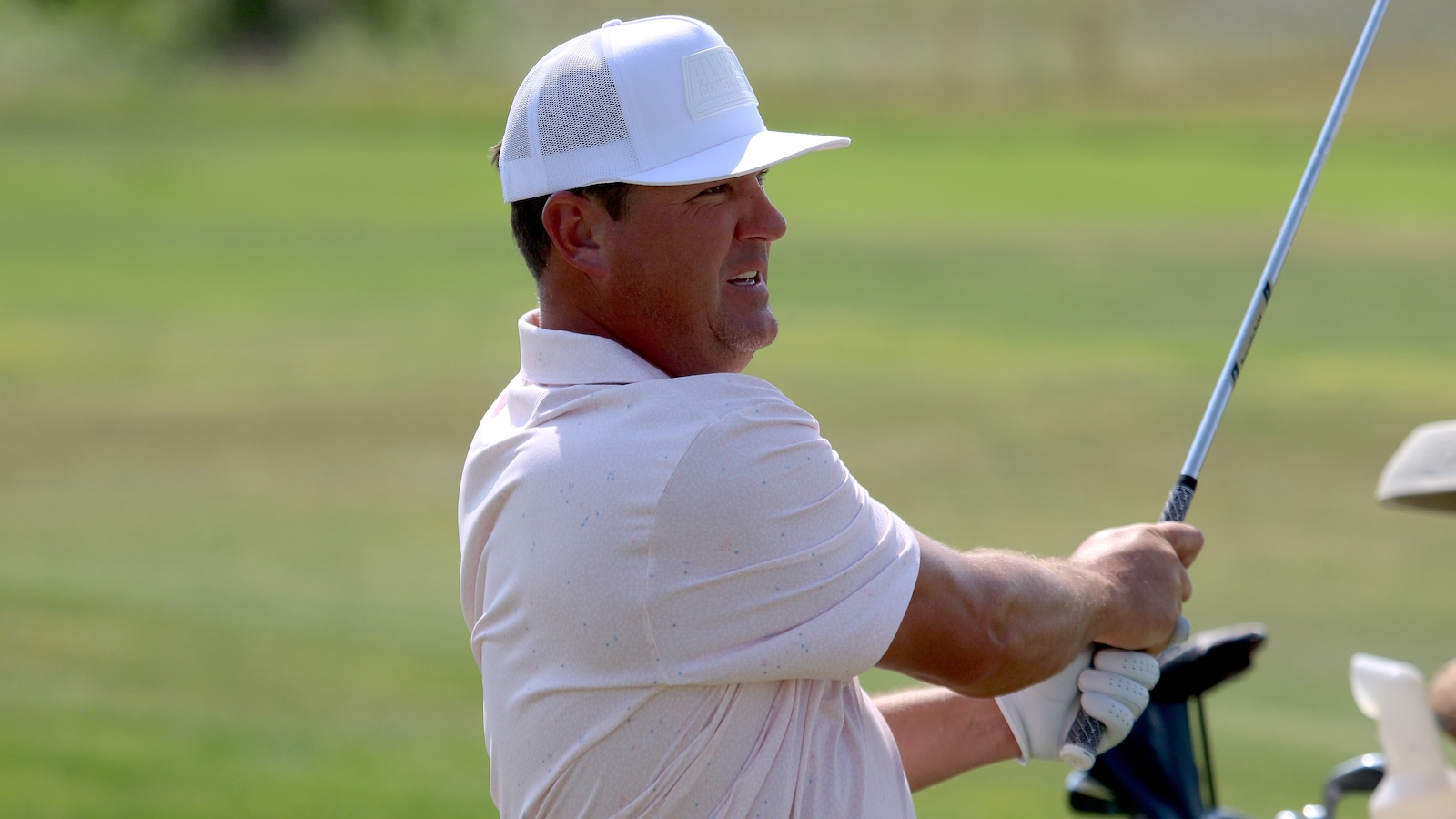Golfer in a white cap and polo shirt mid-swing on a sunny golf course