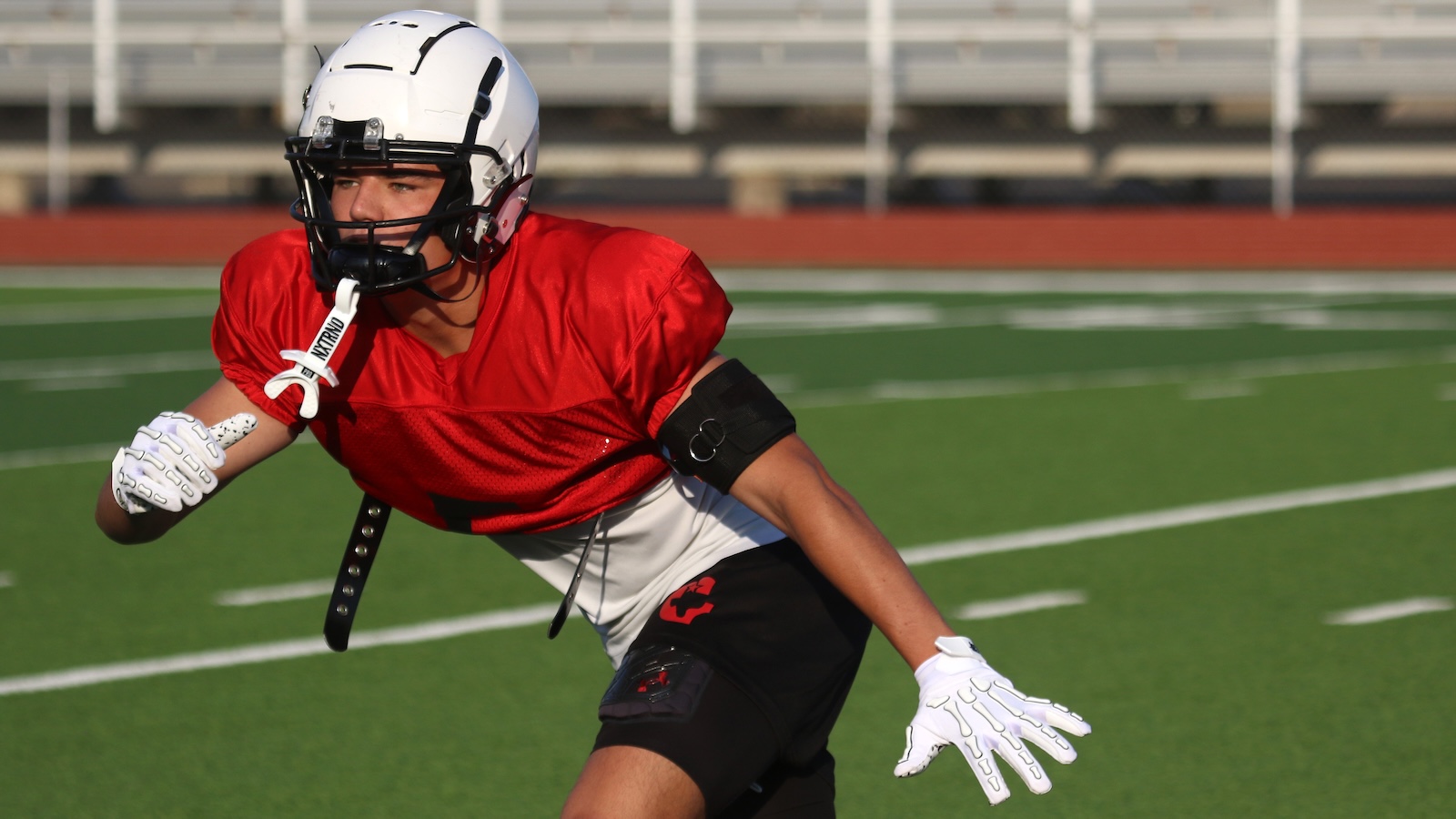 Football player in a red jersey and white helmet sprinting on a green turf football field.