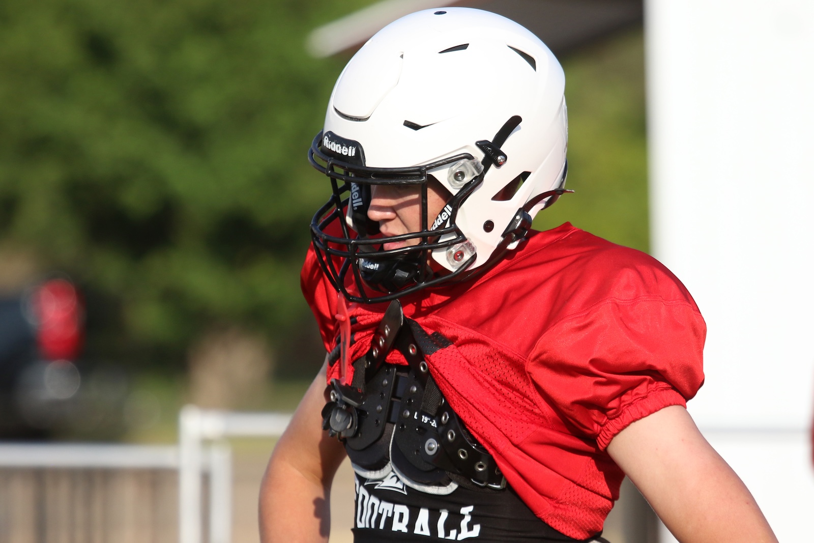 Young football player in a red jersey and white helmet with a black facemask, ready to sprint on the field.