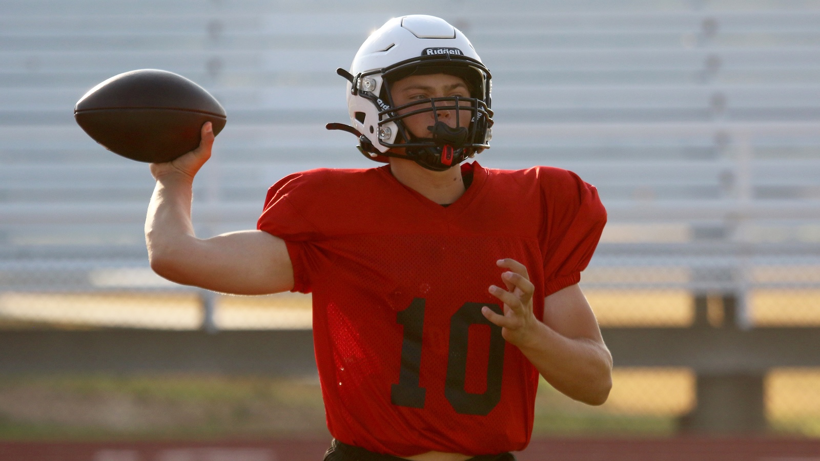 American football quarterback in a red jersey with number 10, mid-throw on an outdoor field with a football in his hand
