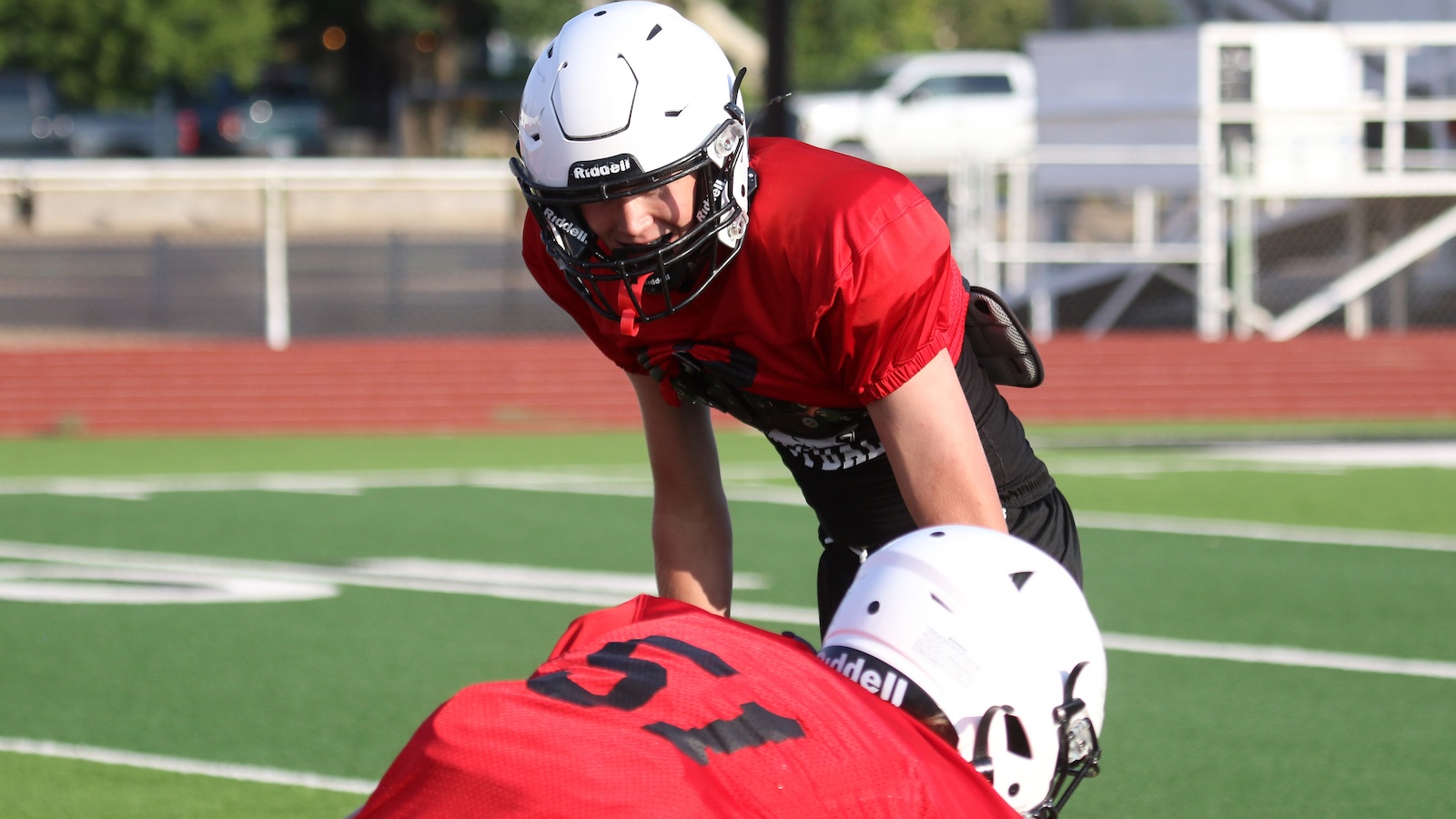 Two football players in red jerseys and white helmets collide on a green field during a play.