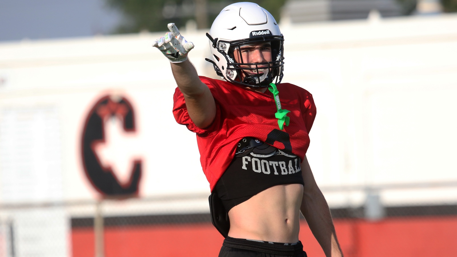 Football player in a red jersey and white helmet points forward during practice on a sunny field.