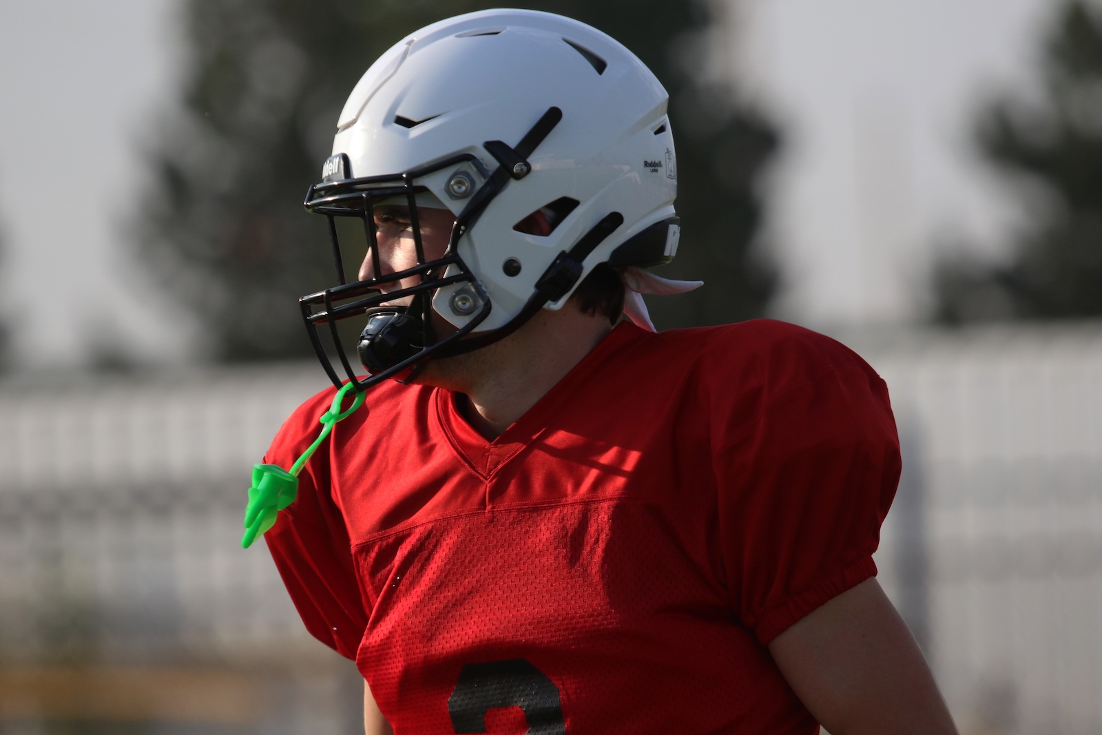 Football player in a red jersey and white helmet, looking to the left on a practice field.