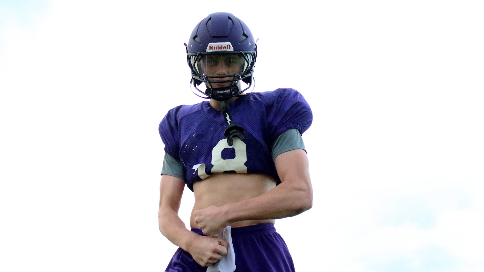 Male football player in a purple uniform and helmet (number 8) flexing his midriff outdoors.