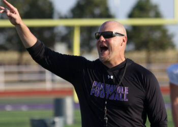 1K6A1180 | Press Pass Sports Coach on a football field raising his arm and pointing, wearing a black long-sleeve shirt and sunglasses.