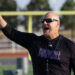 1K6A1180 | Press Pass Sports Coach on a football field raising his arm and pointing, wearing a black long-sleeve shirt and sunglasses.