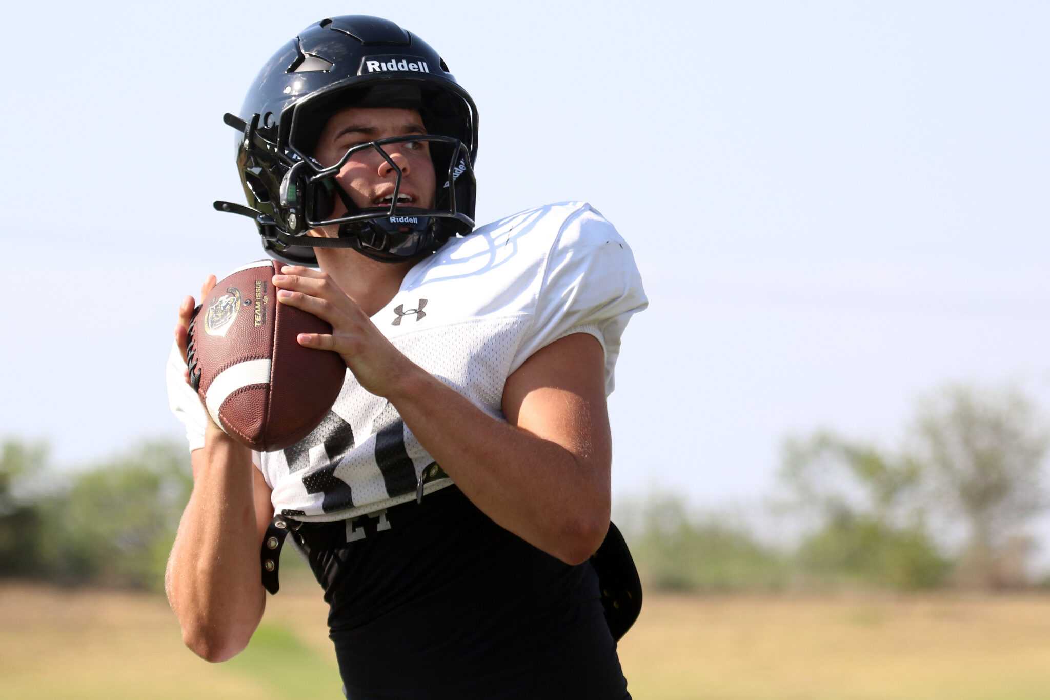 Canadian - Weston Mitchell 4 | Press Pass Sports Football player in a helmet grips a football outdoors, ready to throw on a sunny day.
