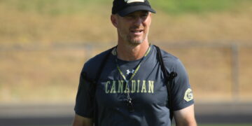 Coach outdoors wearing a navy CANADIAN shirt, black cap, and lanyard.