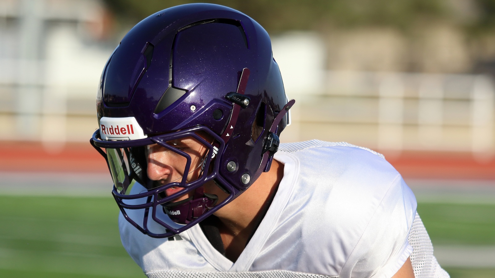 American football player in a white jersey wearing a purple Riddell helmet on a sunny practice field
