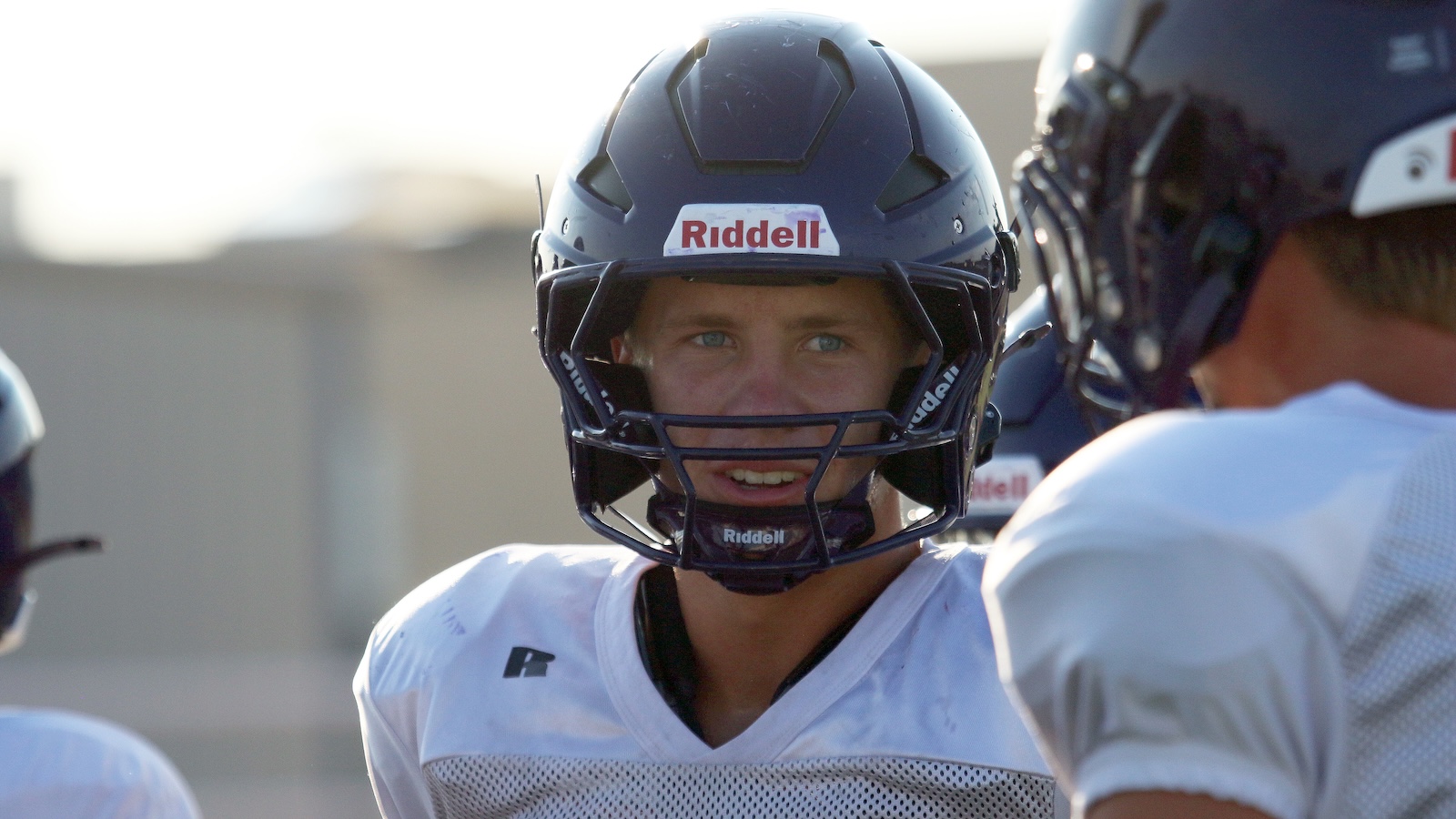 Close-up of a football player wearing a dark blue Riddell helmet with faceguard, looking ahead during practice.