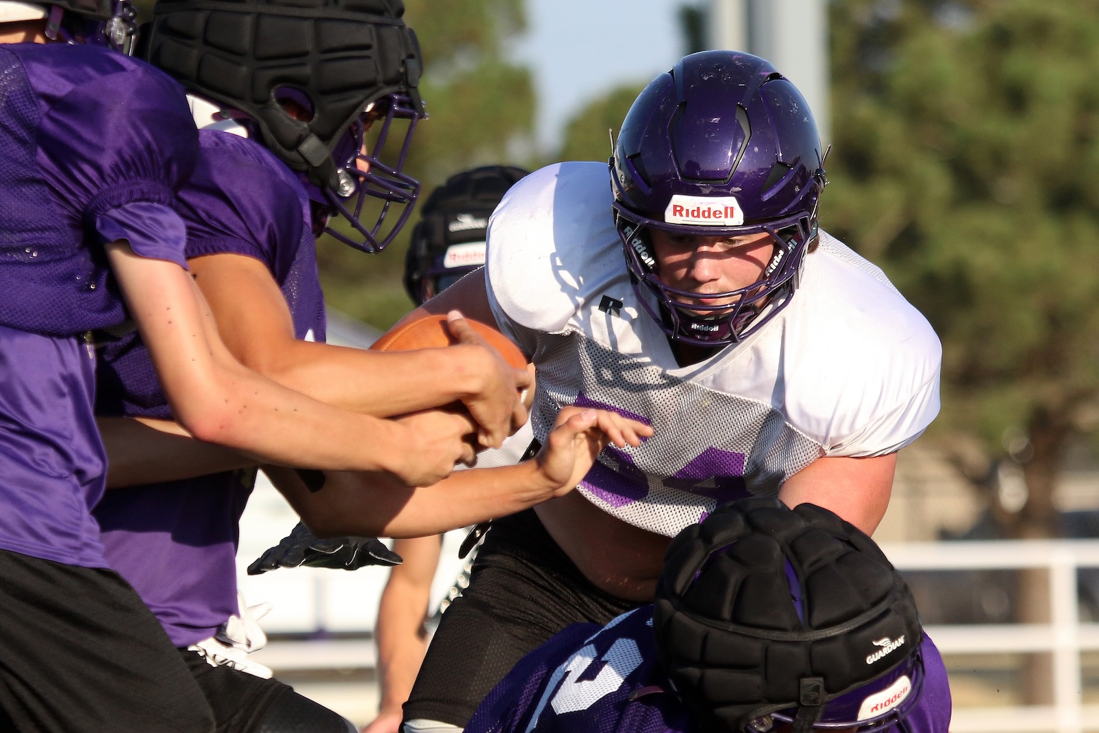 American football players wearing purple and white jerseys clash at the line of scrimmage during a play in action.