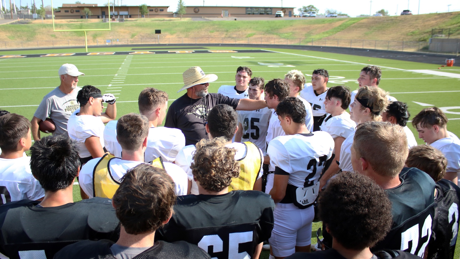 Football coach addresses a huddle of players on a sunny practice field on the stadium turf