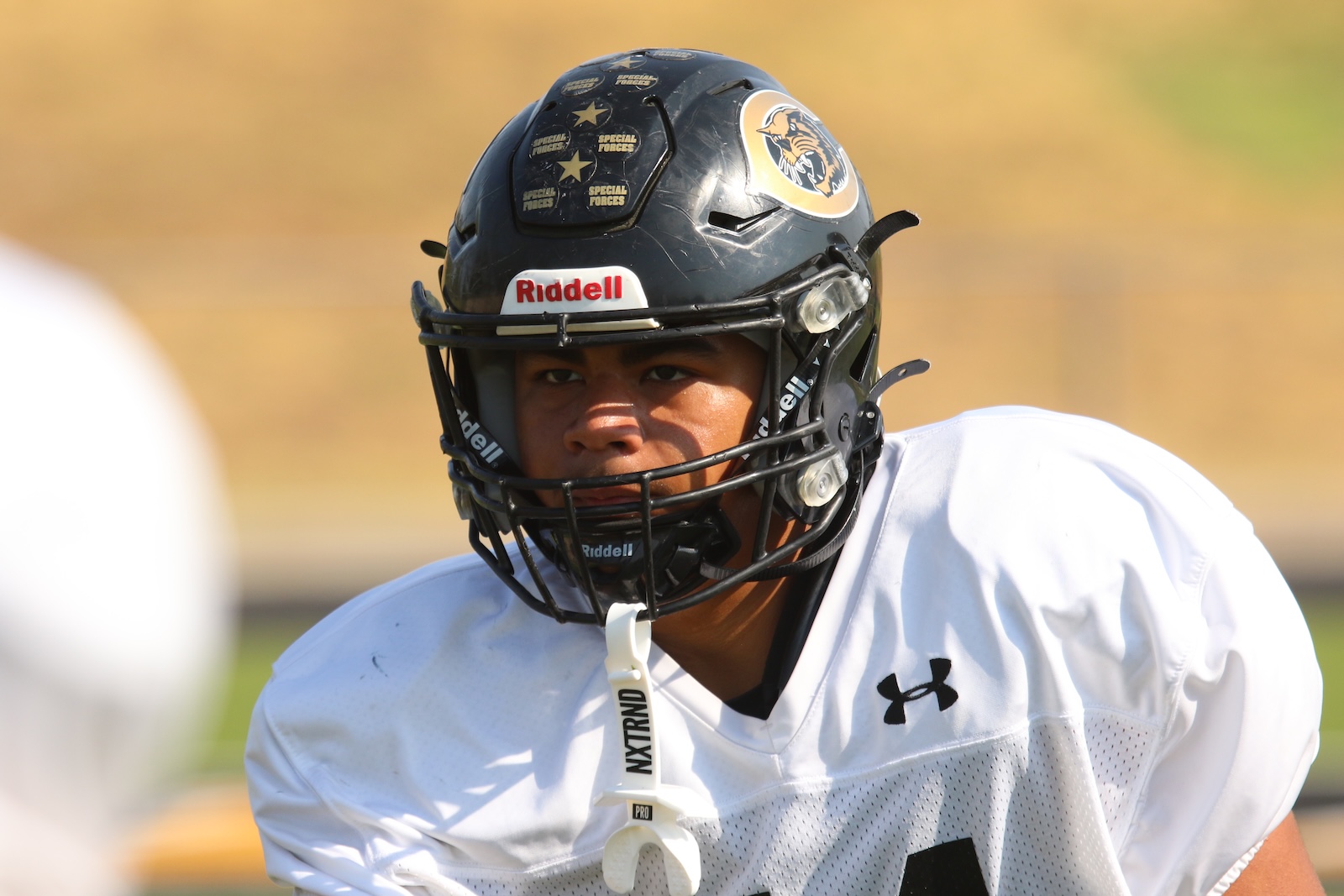 Football player in a helmet and white jersey during practice, focused on the play.