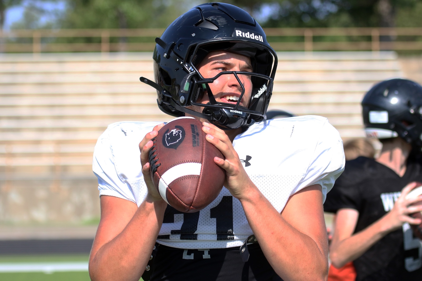 Football player in a white jersey grips a football, preparing to throw.