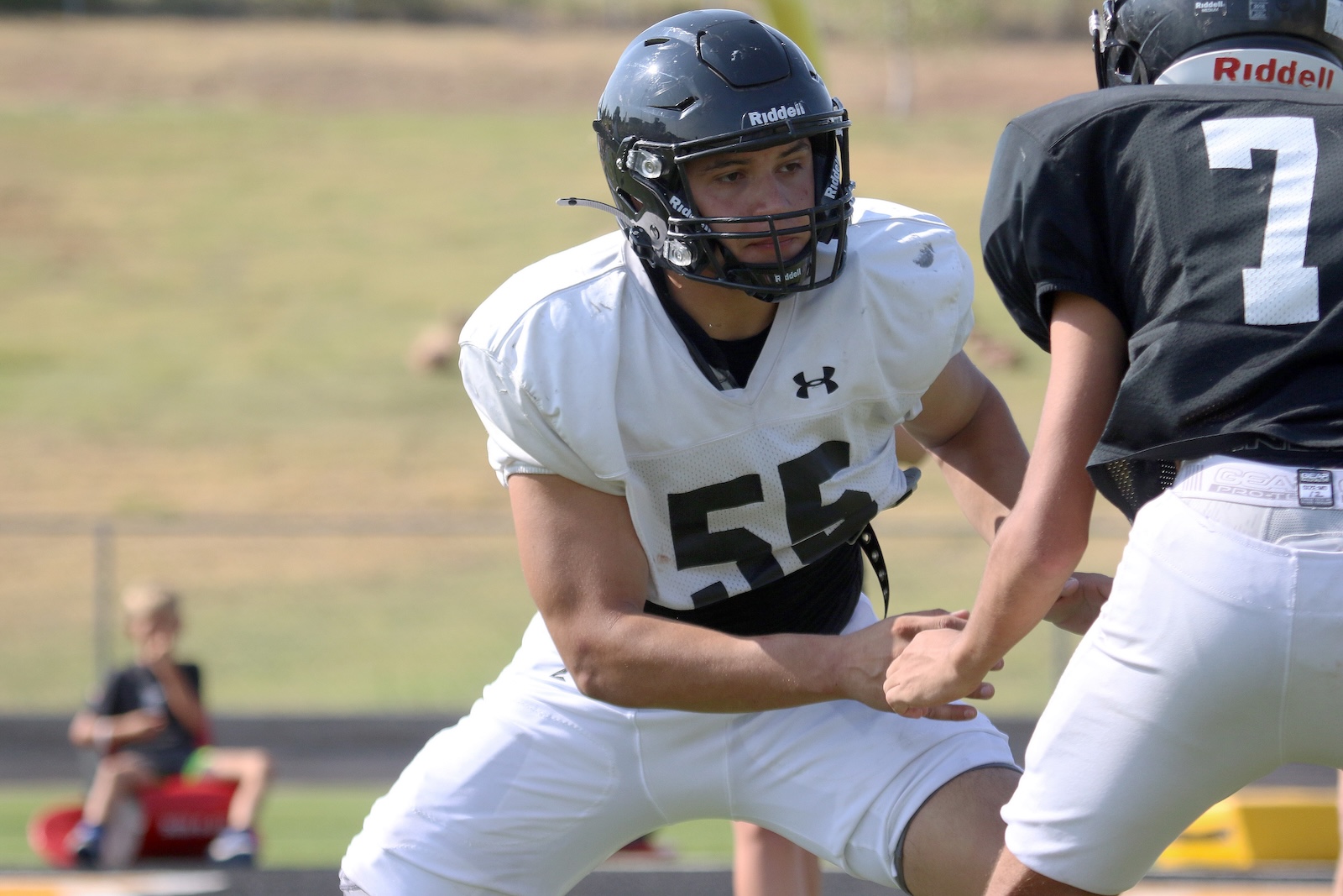 Football players in a street-style field; player in white jersey #53 guards and blocks during play with a black helmet on.