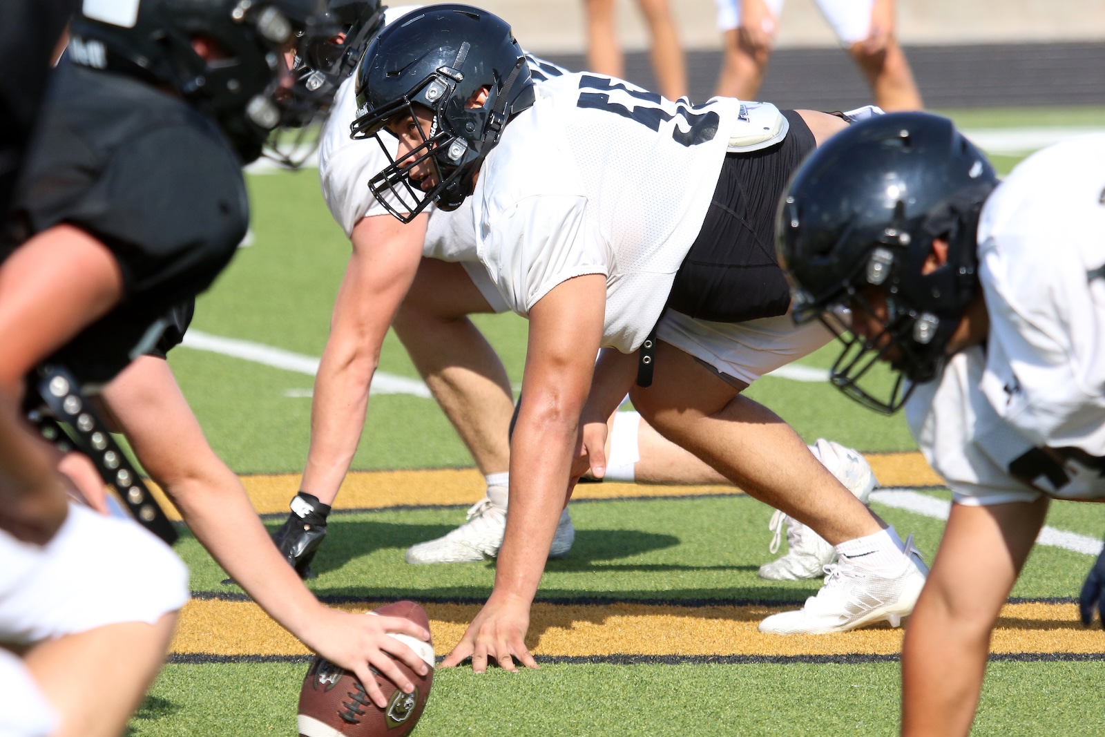 Football linemen at the snap on a turf field, center hand on the ball ready to hike.