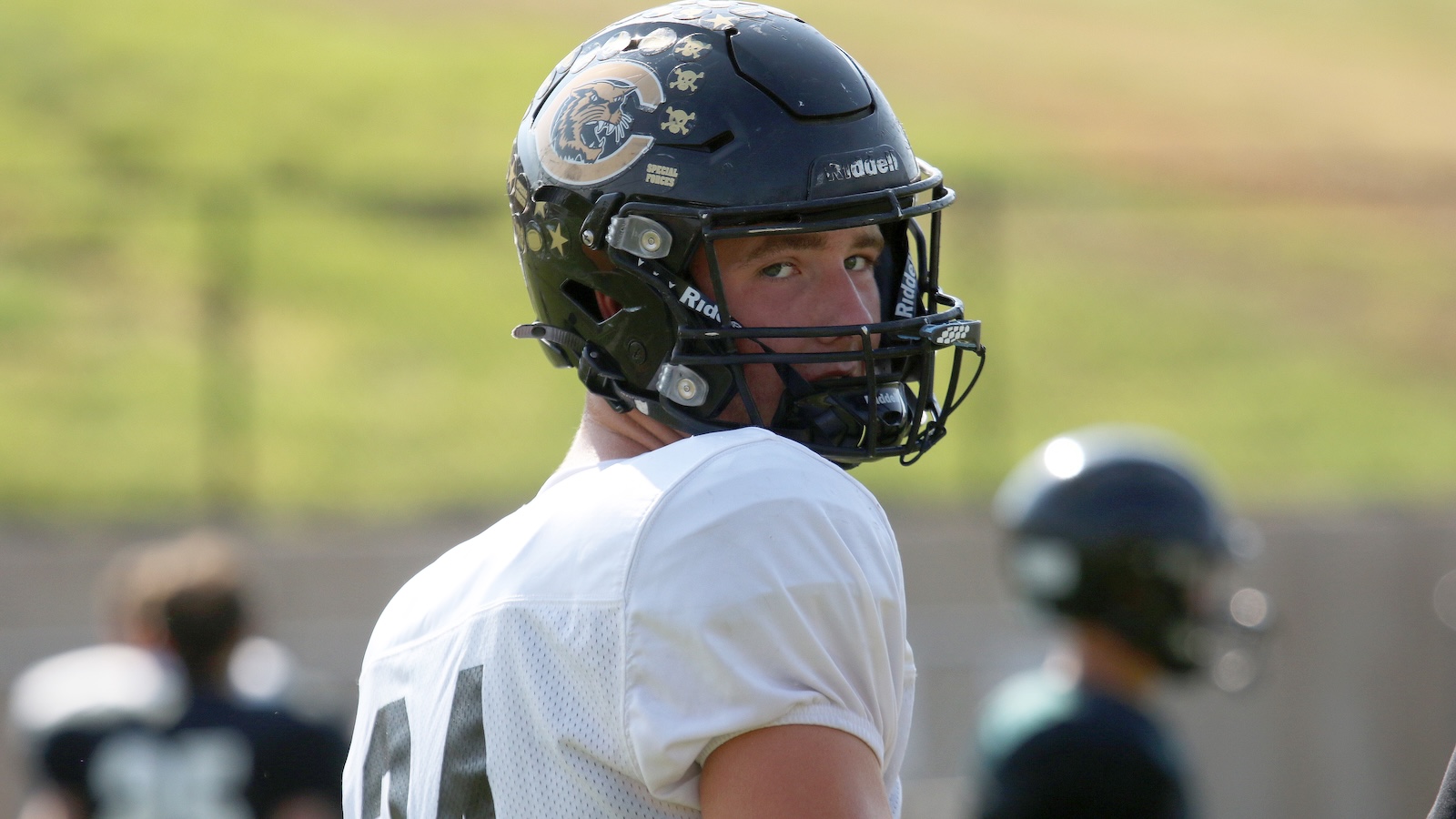 Football player in a white jersey wearing a black helmet, looking back over his shoulder on the field