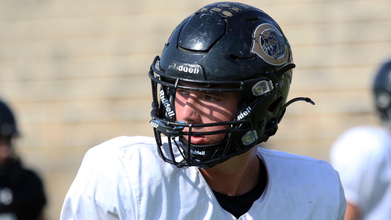 Football player in a black Ridell helmet and white jersey, looking to the left.