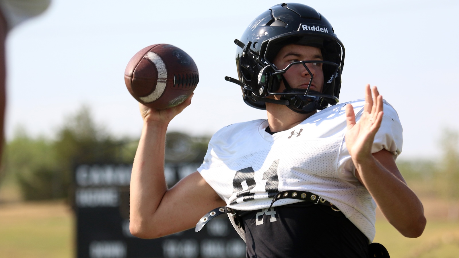 Football quarterback in a white jersey and black helmet preparing to throw a pass on an outdoor field