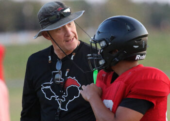 Shallowater - HC Rodney Vincent 2 | Press Pass Sports Two people on a grassy field share a hug; one in a black shirt with a graphic, gray hat and sunglasses, the other in a red jersey with a black helmet.