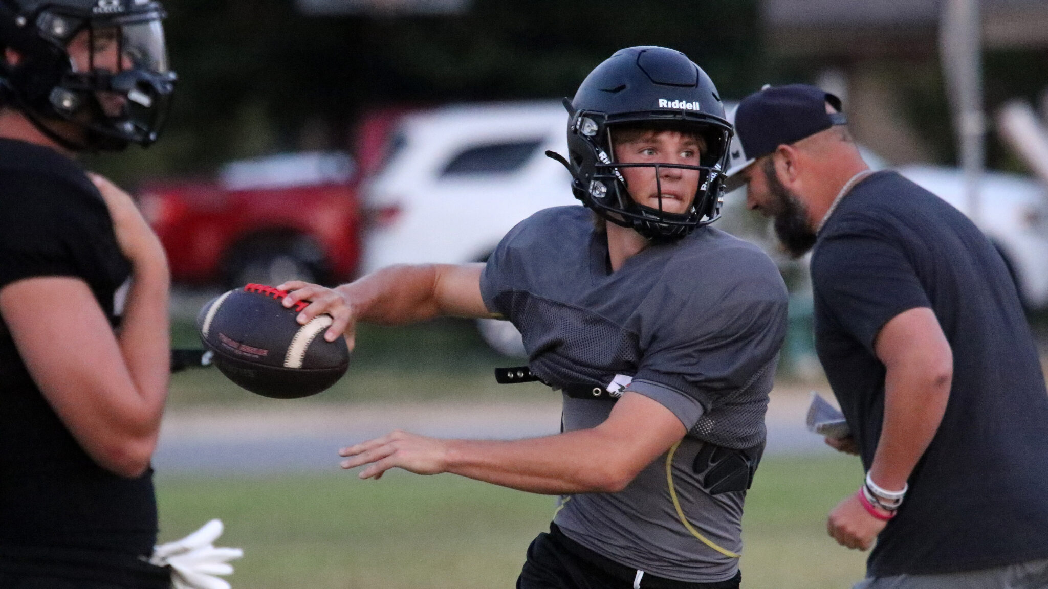 1K6A4466 | Press Pass Sports Quarterback in gray shirt and helmet throws a football during a drill with teammates nearby