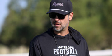 Man in black cap and sunglasses outdoors, wearing a black shirt that reads 'ANTELOPE FOOTBALL' on the front.