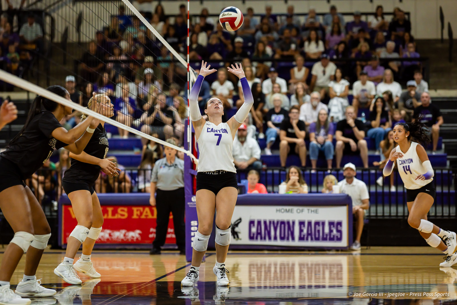 White Canyon player #7 sets the ball over the net as teammates and a full crowd watch.