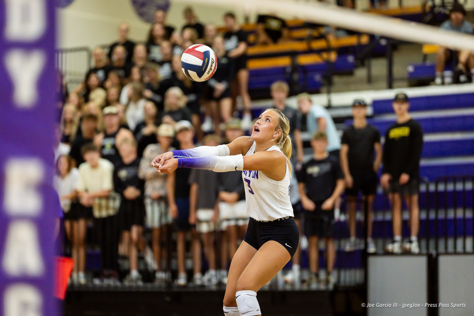 Volleyball player in white jersey sets the ball while crowd watches in a gymnasium.