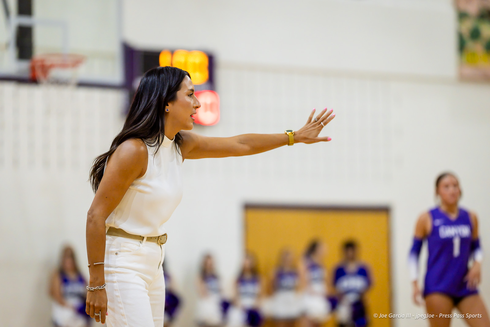 Woman in white outfit on a basketball court extending her arm as she directs or signals to players during a game/coach giving instructions.