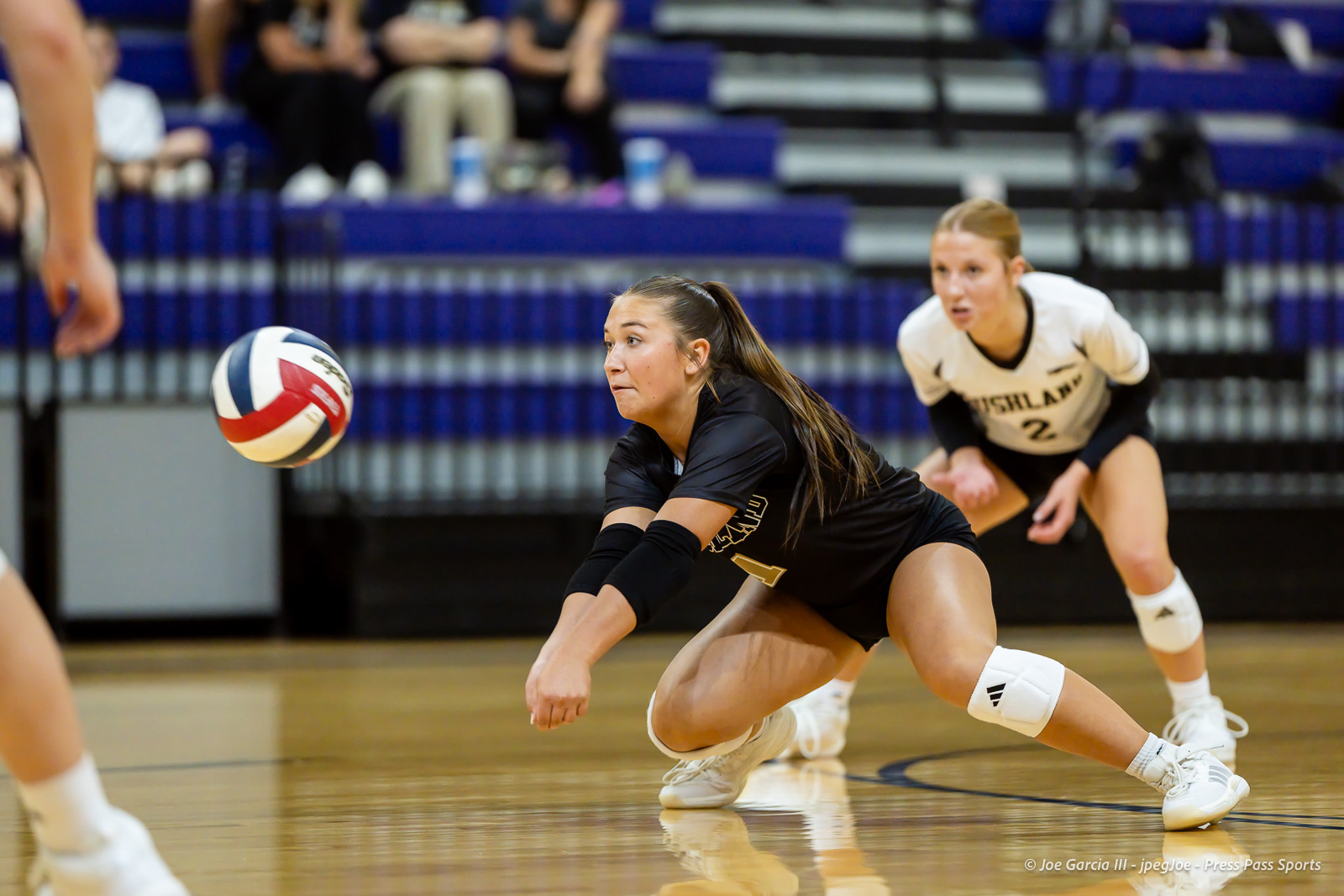 Two female volleyball players dive for the ball during a match in a gym.