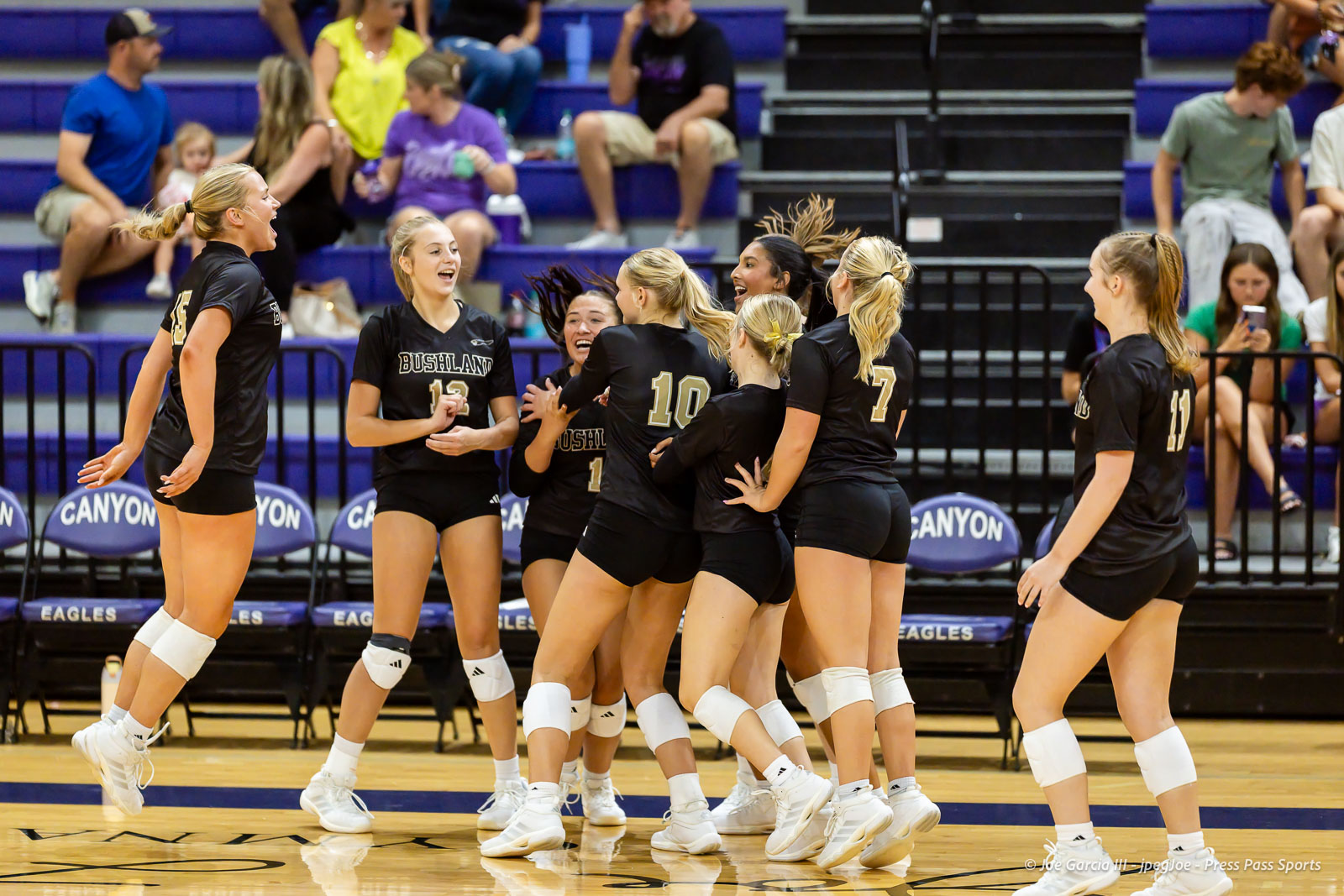 Volleyball team in black uniforms celebrate and cheer together on the gym court.