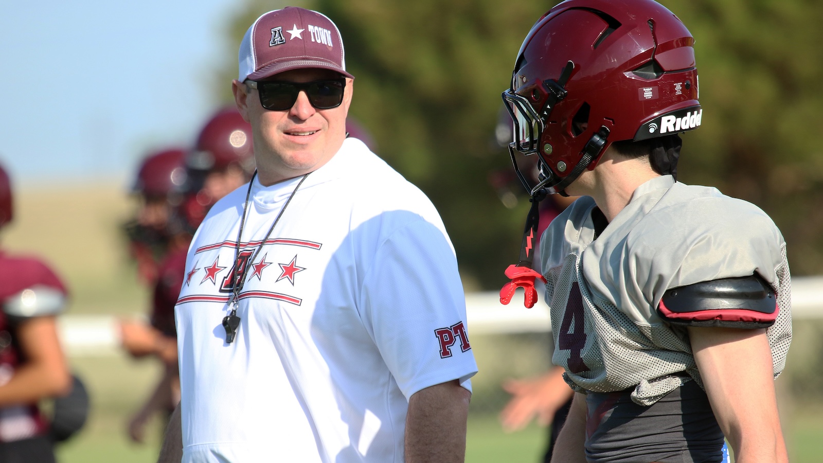Football coach with a whistle talking to players during a practice on the field under sunny skies