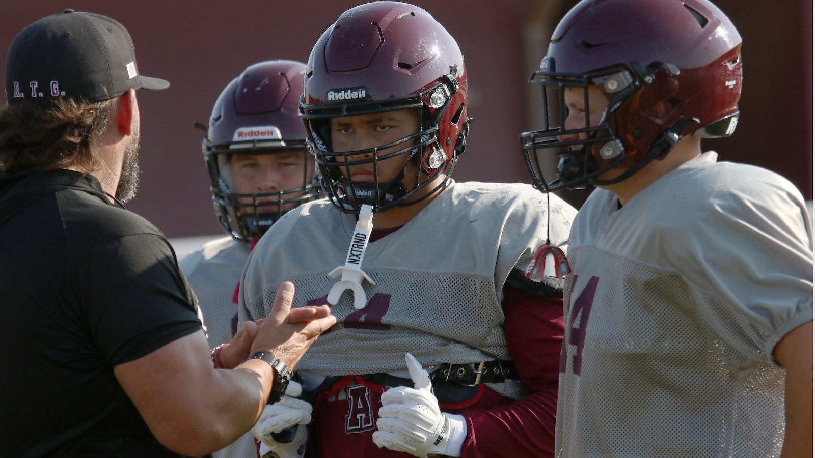 Coach giving instructions to football players in maroon helmets during practice.