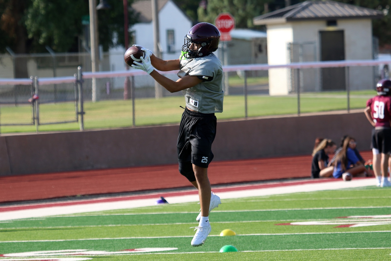 Football player in gray jersey and purple helmet catches a ball mid-air during practice on a turf field.