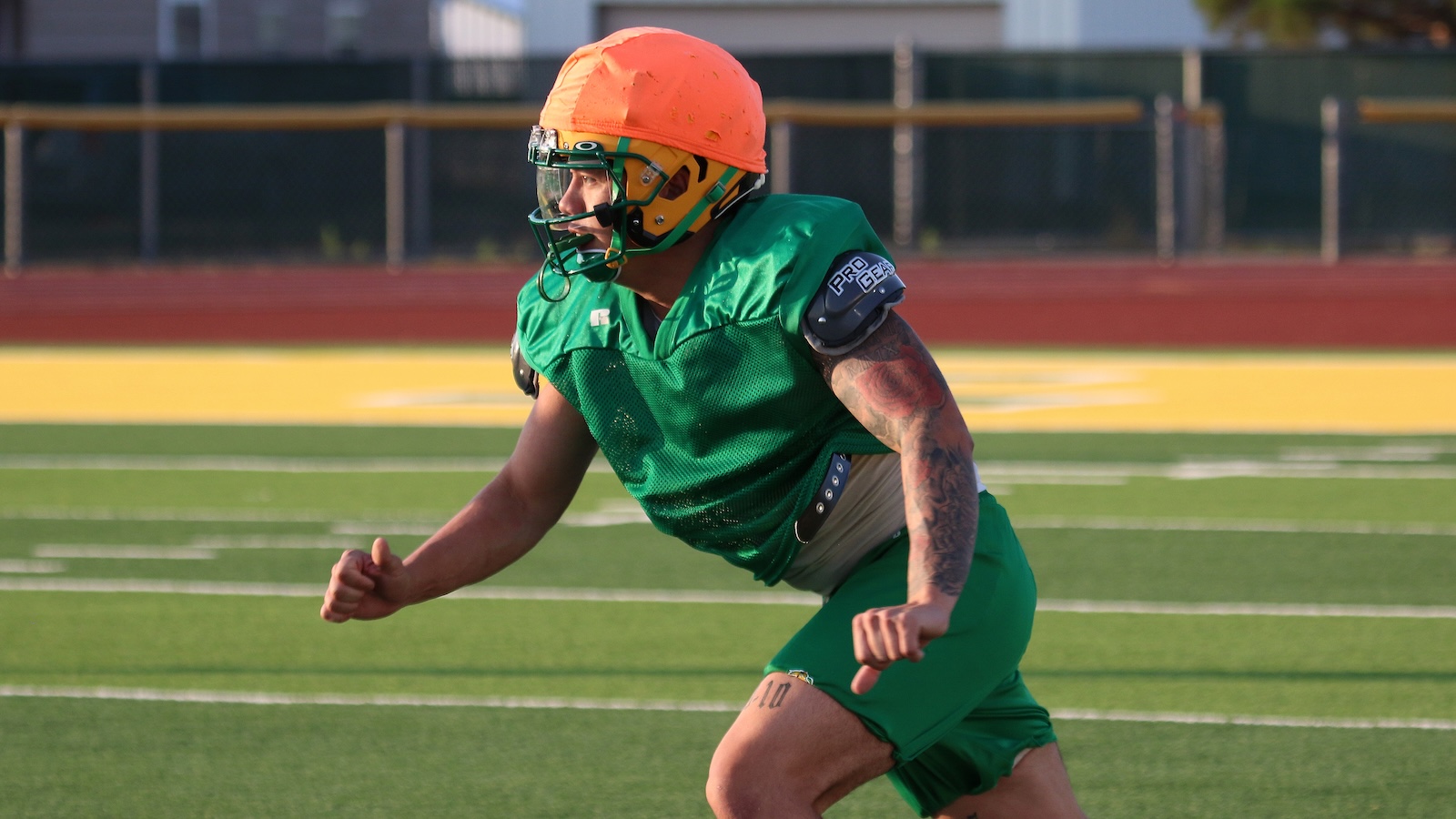 American football player in a green jersey and orange helmet sprinting on a turf field.