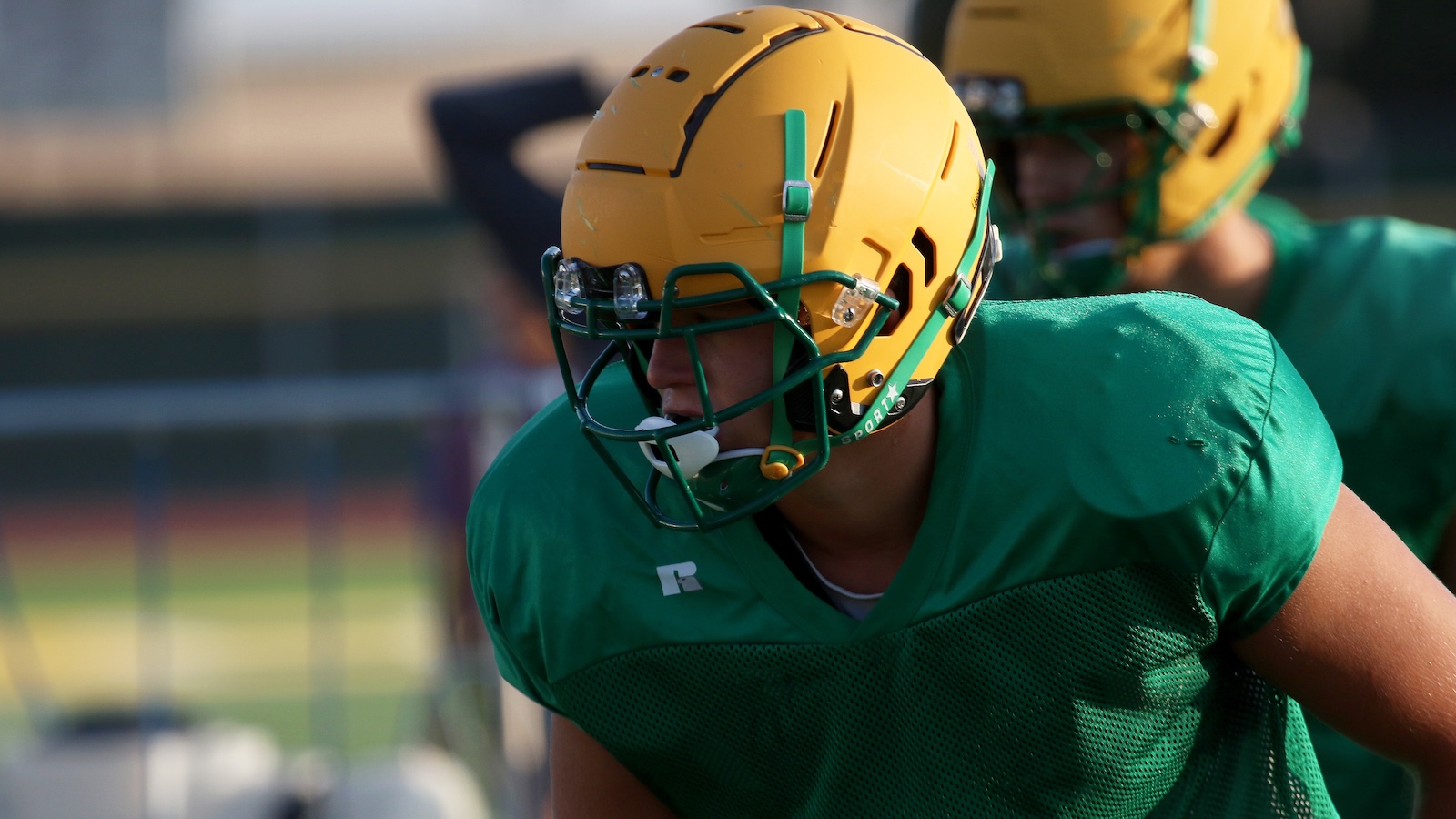 Football player in a green jersey and yellow helmet during practice on a sunny field.