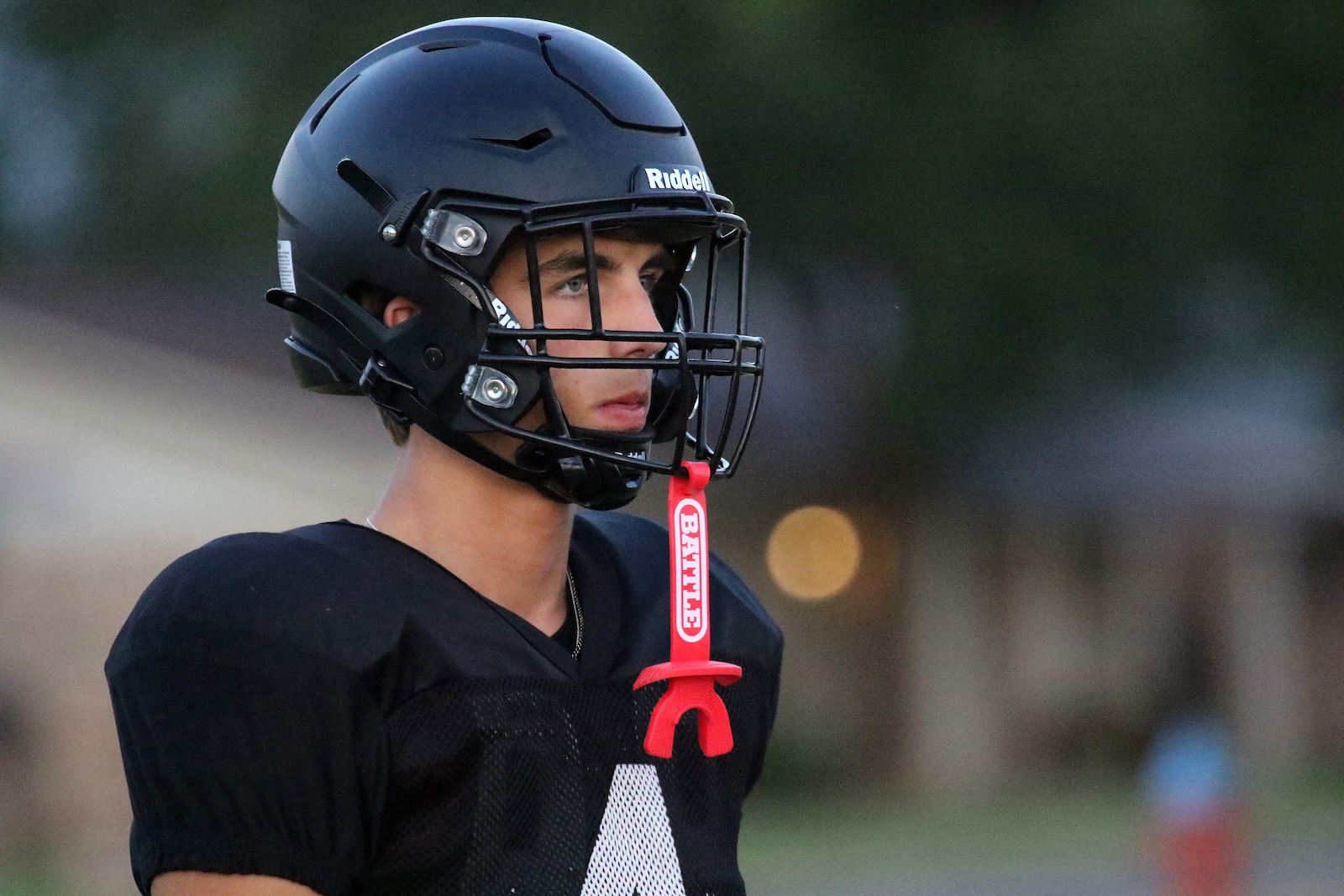 Close-up of a football player wearing a matte black helmet with a facemask and a red mouthguard tether, looking to the right.