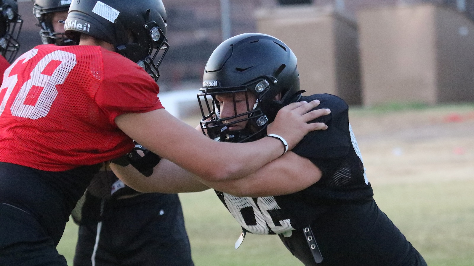 Two football players collide in a blocking drill, one in a red jersey with number 68 pushing against a black-jersey teammate wearing a helmet.