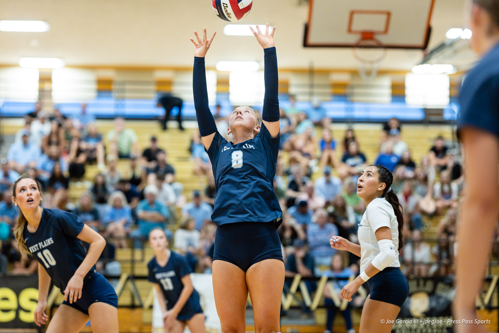 west-plains-vs-amarillo-high-2026-jpegJoe-pps-1 | Press Pass Sports Volleyball player in navy #8 reaches overhead to contact a ball as the gym audience watches from the bleachers.