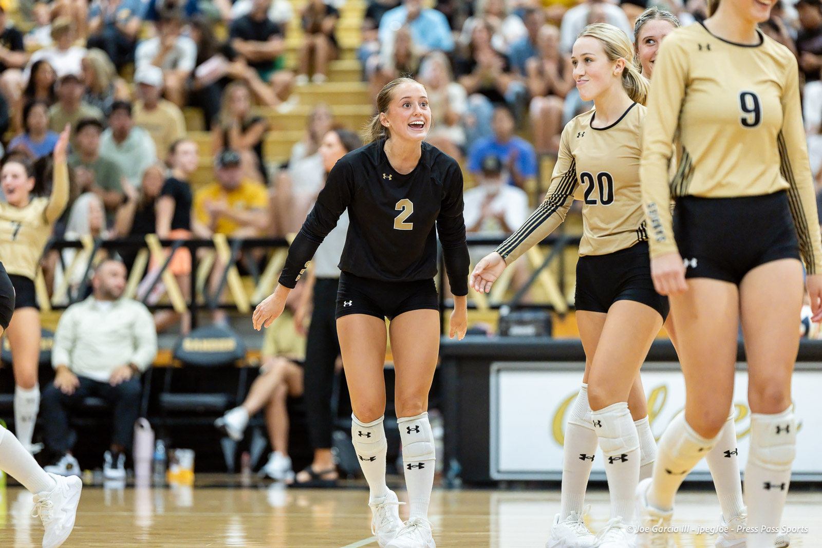 west-plains-vs-amarillo-high-2026-jpegJoe-pps-9 | Press Pass Sports Volleyball players on the court celebrate; a player in black with number 2 smiles as teammates in beige jerseys (numbers 20 and 9) stand nearby, cheering crowd in the stands behind.