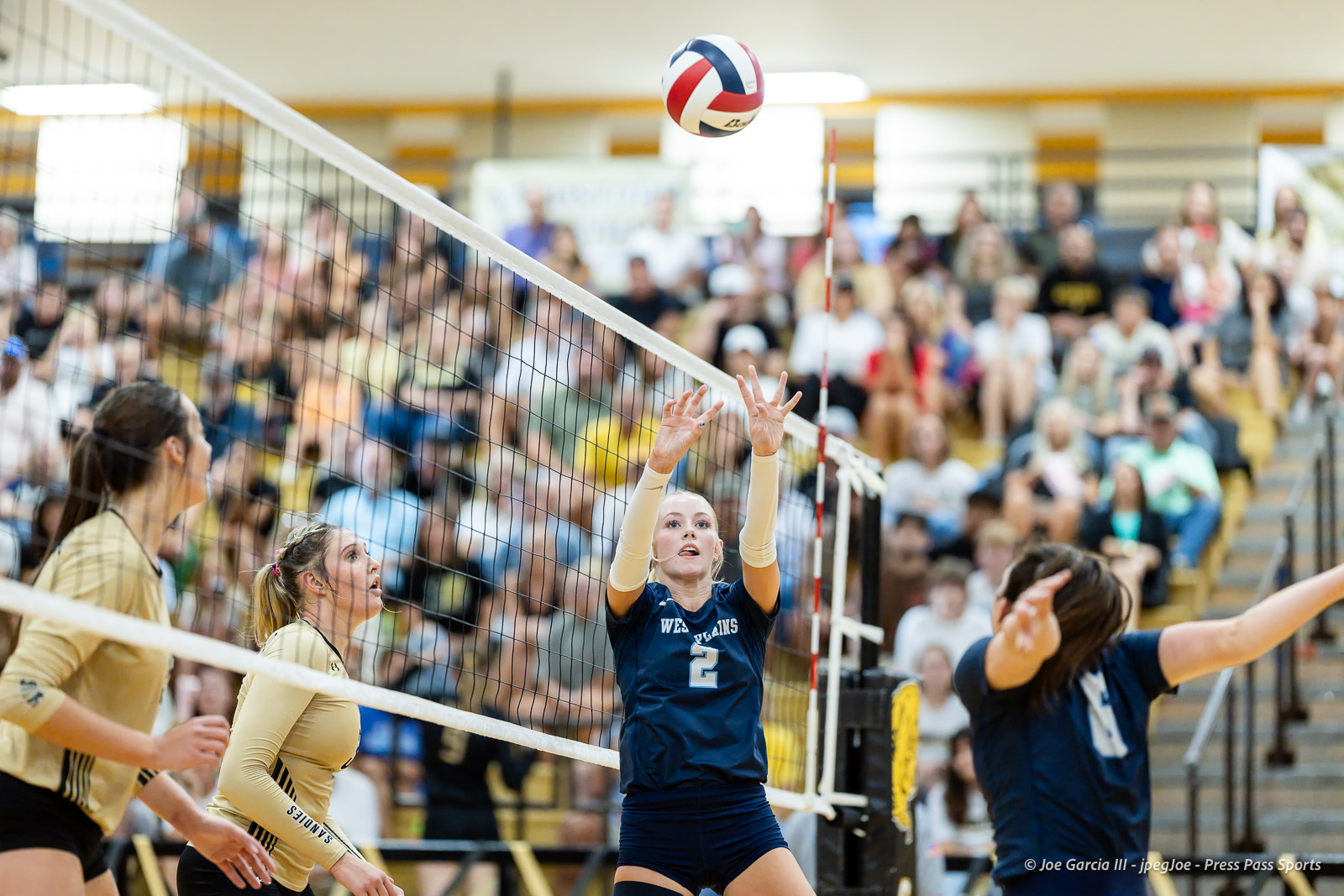 west-plains-vs-amarillo-high-2026-jpegJoe-pps-13 | Press Pass Sports Female volleyball players at the net during a match; a blue-jersey player (#2) reaches up to block the ball as a crowded gym watches.