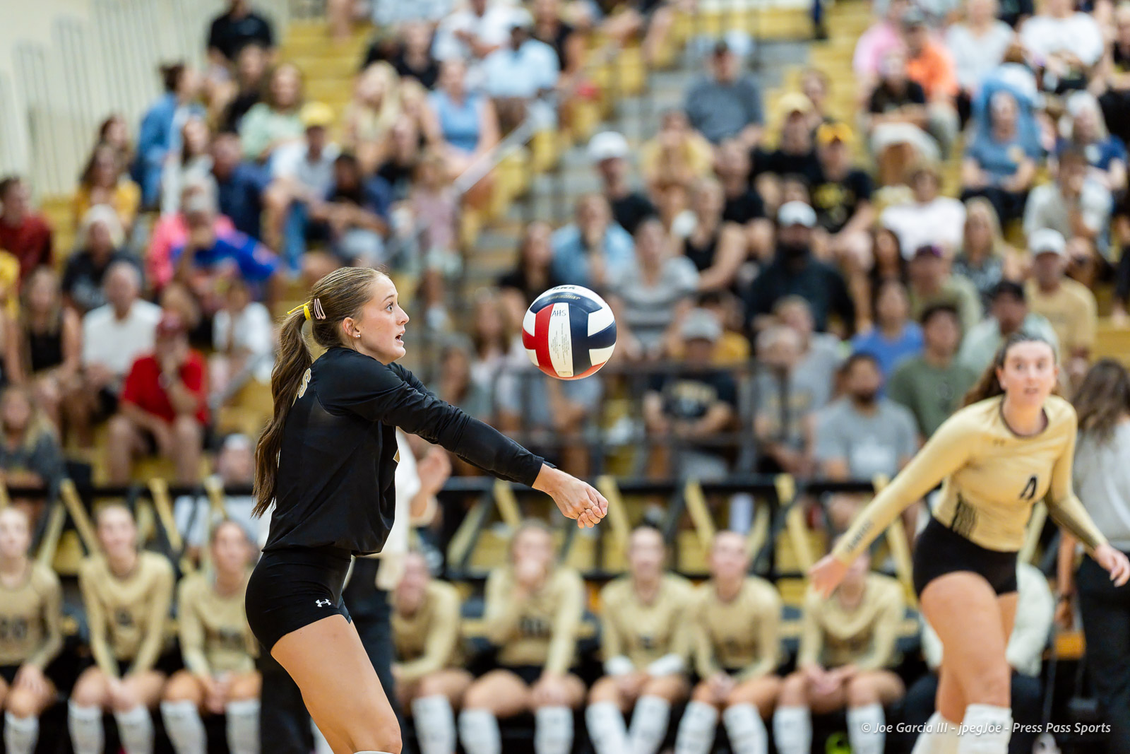 west-plains-vs-amarillo-high-2026-jpegJoe-pps-11 | Press Pass Sports Female volleyball player in a black uniform extends her arms to receive a ball during a crowded indoor match, with a cheering gym audience in the background.