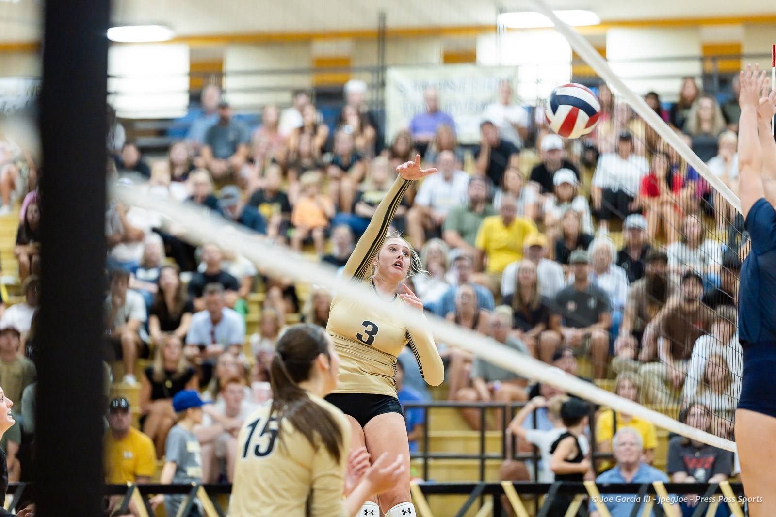 west-plains-vs-amarillo-high-2026-jpegJoe-pps-12 | Press Pass Sports Female volleyball player in a beige jersey #3 leaps to spike the ball near the net as a large crowd watches from the bleachers in a gymnasium onlookers