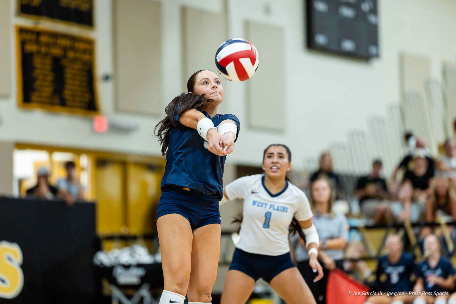 west-plains-vs-amarillo-high-2026-jpegJoe-pps-23 | Press Pass Sports Female volleyball players in a gym, one in blue reaching to bump a red, white, and blue ball midair as spectators watch.