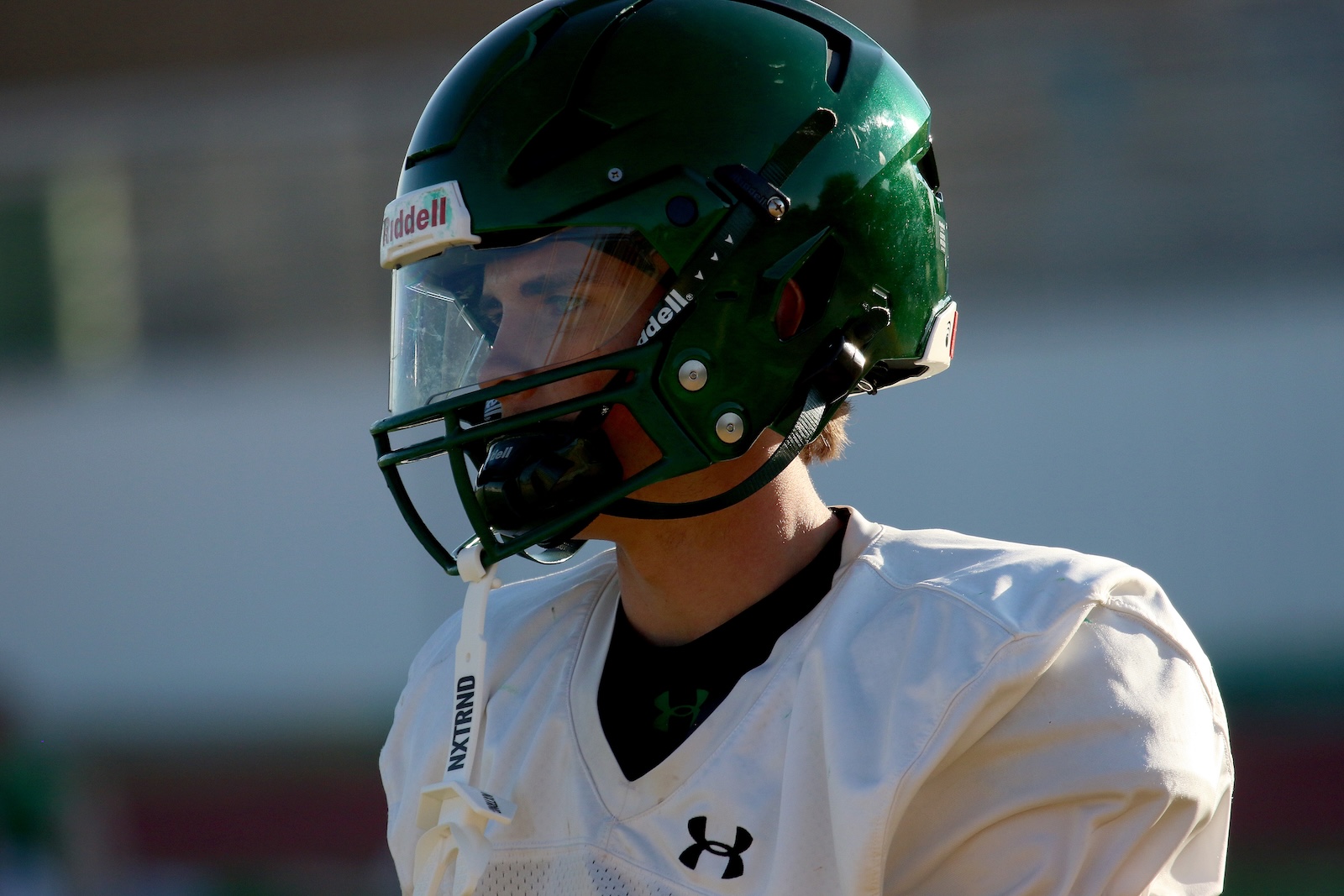 Football player in a green helmet and white jersey, facing left, during practice or game.