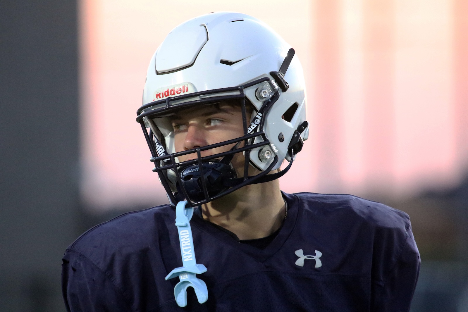 Male football player wearing a light-blue Riddell helmet and navy jersey, looking to the side during practice.
