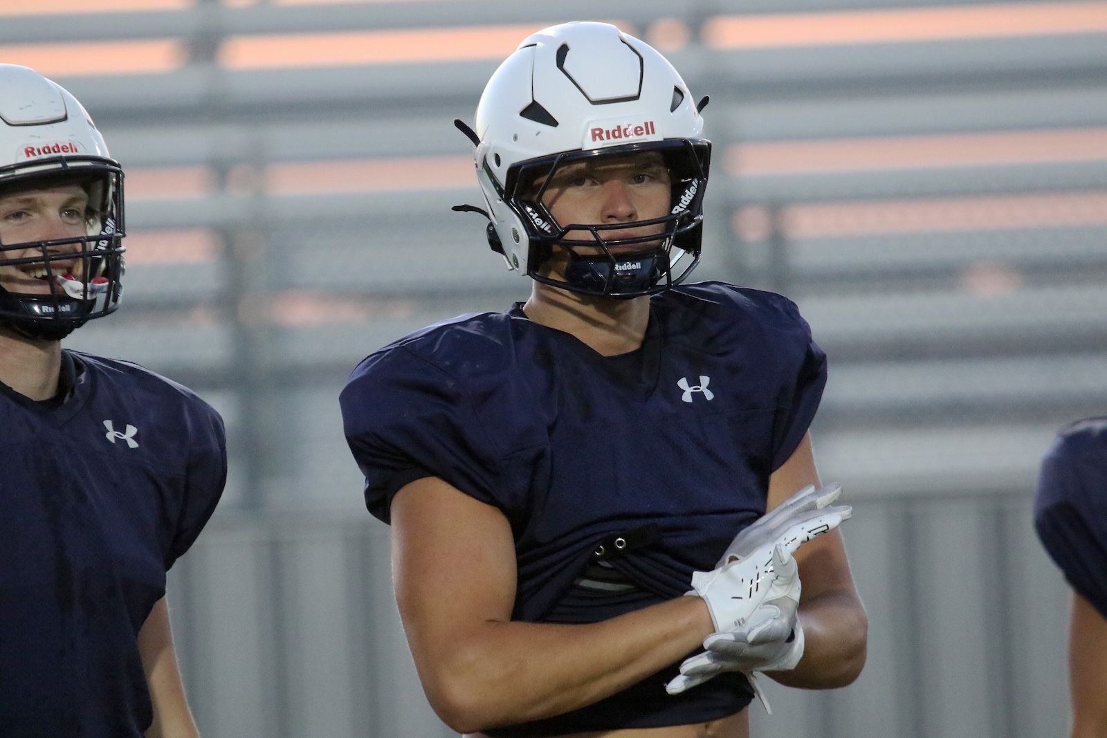 Two football players in navy practice jerseys and white helmets on a field, foreground player with arms crossed.