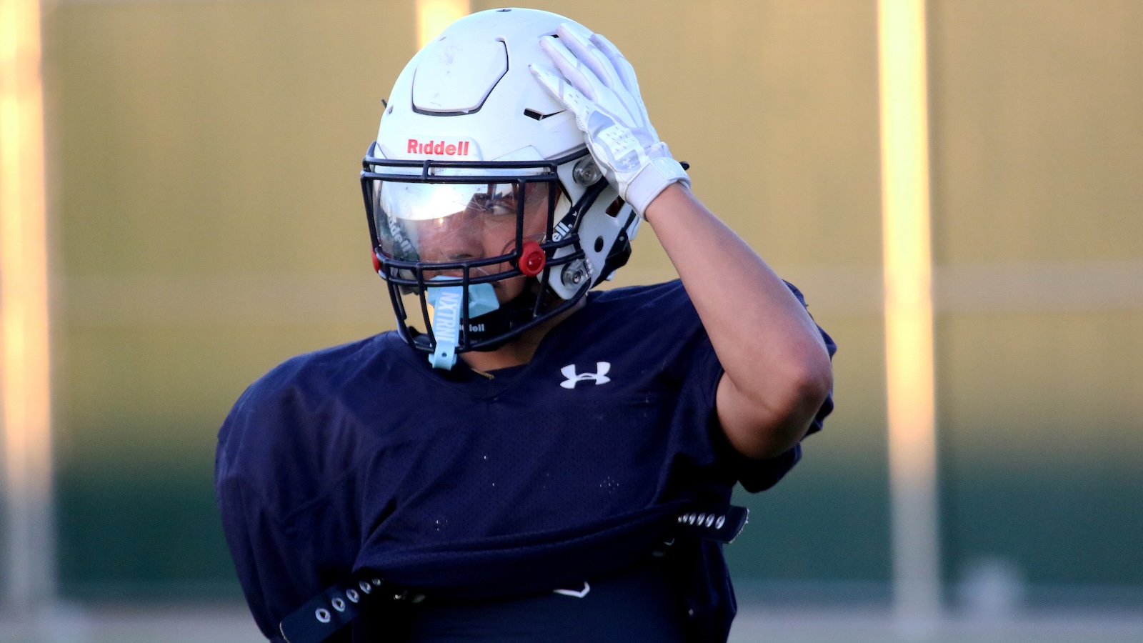 Football player in navy jersey saluting with his white helmet, on a sunny field