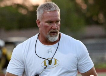 Amarillo High - HC Chad Dunnam 2 | Press Pass Sports Middle-aged man with gray hair and beard wearing a white athletic shirt, sunglasses on a cord around his neck, outdoors at a sports field.