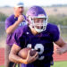 1K6A8921 | Press Pass Sports Football player in a purple jersey carrying a football while running on a track field, helmet on